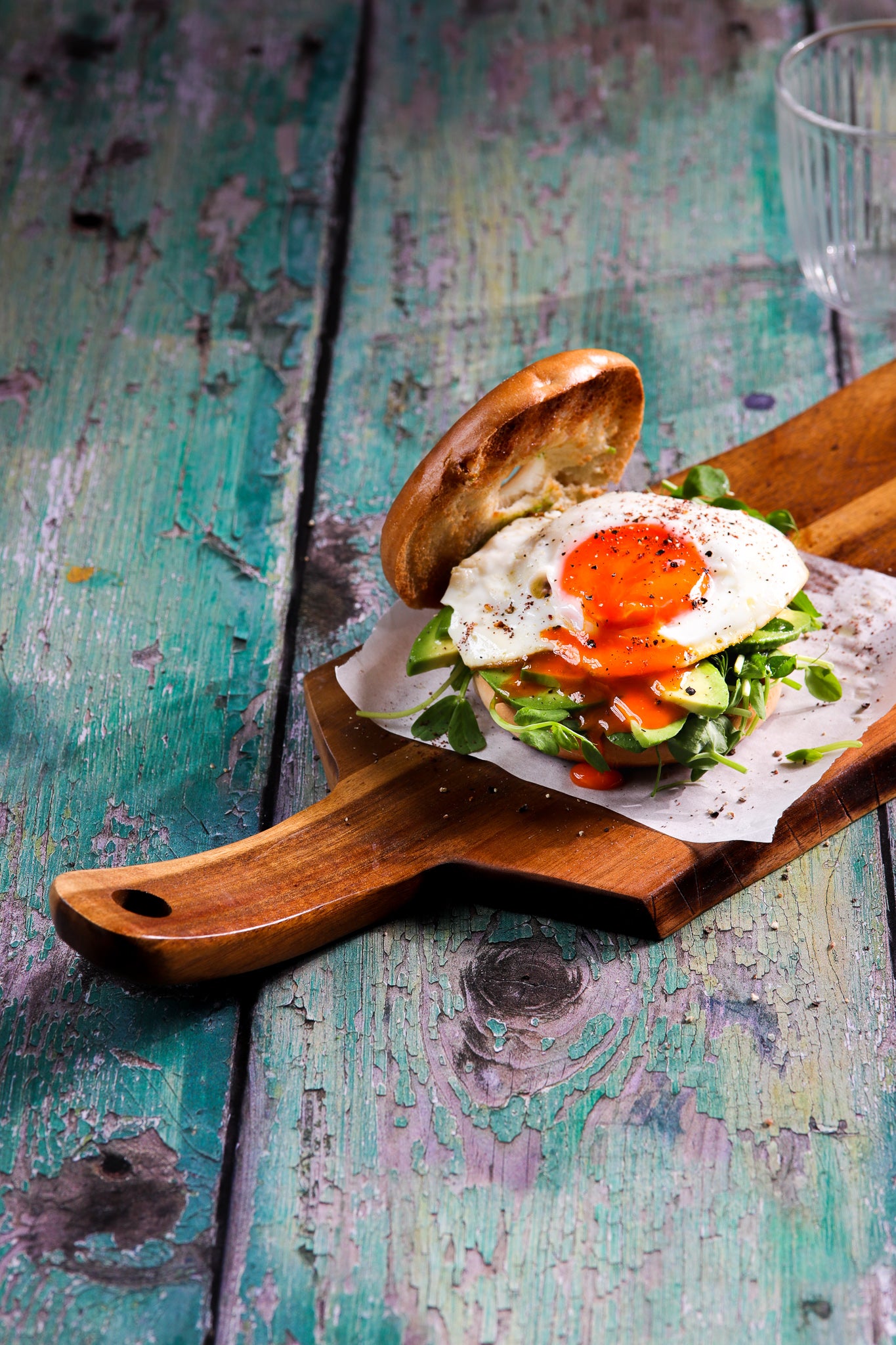 A board with an open egg burger styled on a green flaky wood plank effect vinyl photography backdrop with a textured surface.