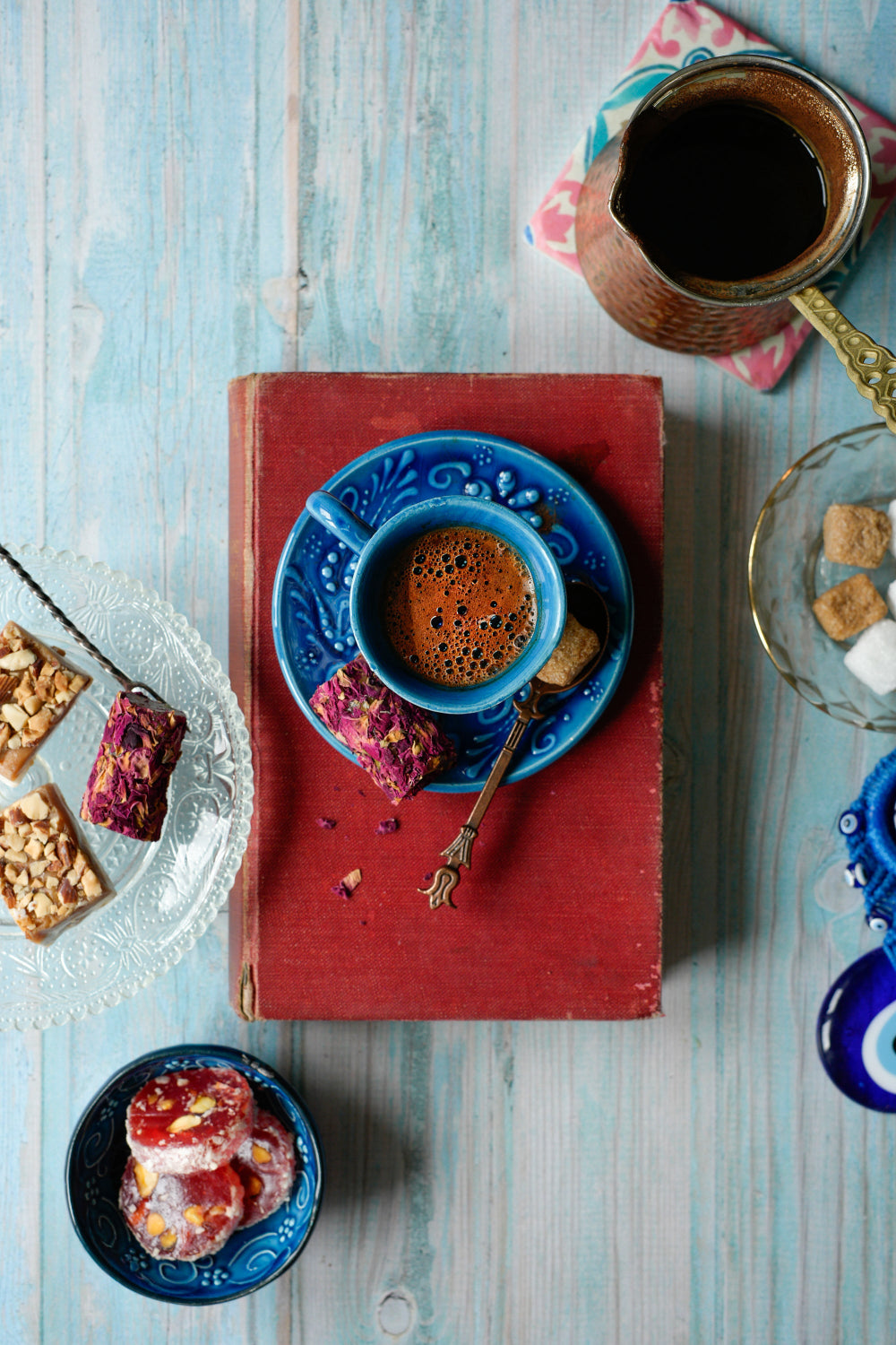 Cup of Turkish coffee on a red antique book with Turkish delight styled on a weathered wood-effect vinyl photography backdrop in a soft turquoise.