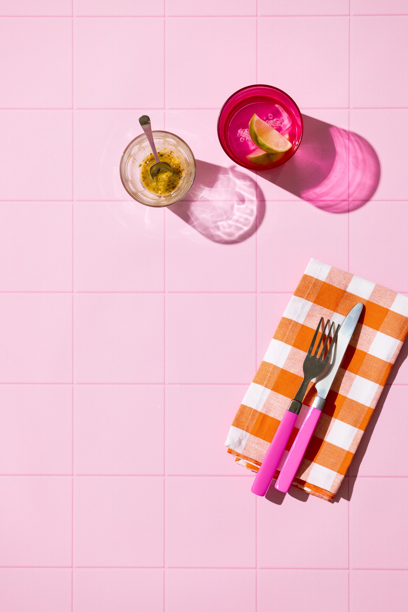 Colourful glassware, checked napkin pink cutlery on a pink tile background