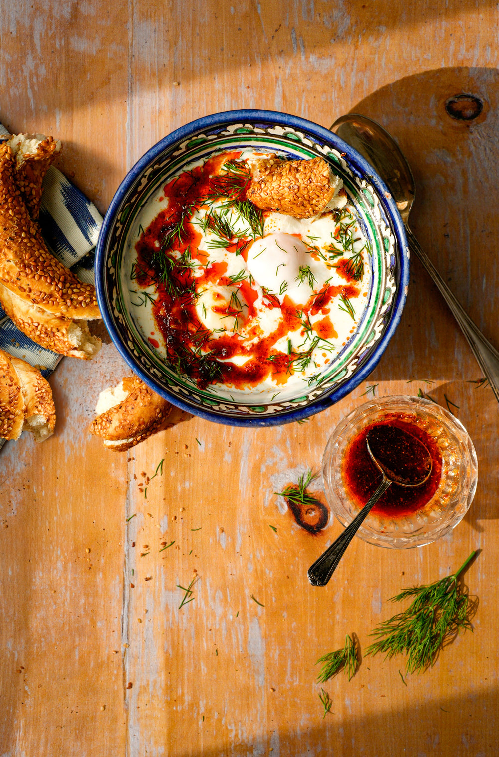 Bowl of Çılbır: -Turkish Poached Eggs styled on a honey pine wood-effect vinyl photography backdrop with natural knots and fading.