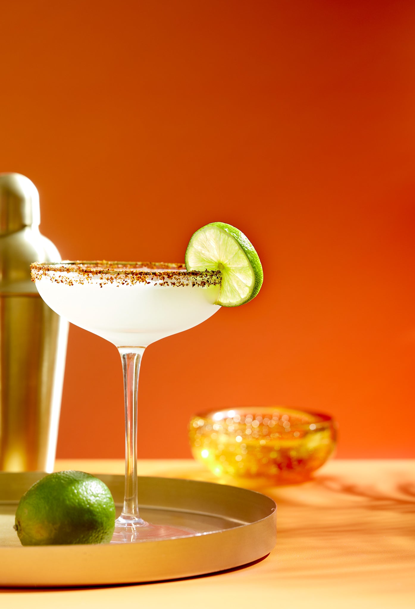 Cocktail with lime garnish on an orange background