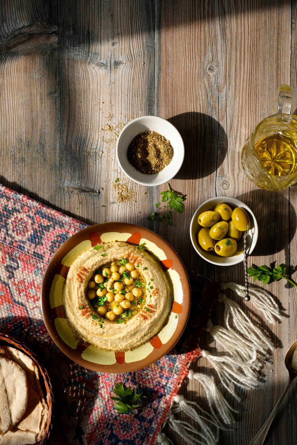 Traditional hummus dish with olives and bread styled on a rustic photography backdrop with a contrasting natural striped woodgrain in beige and browns.