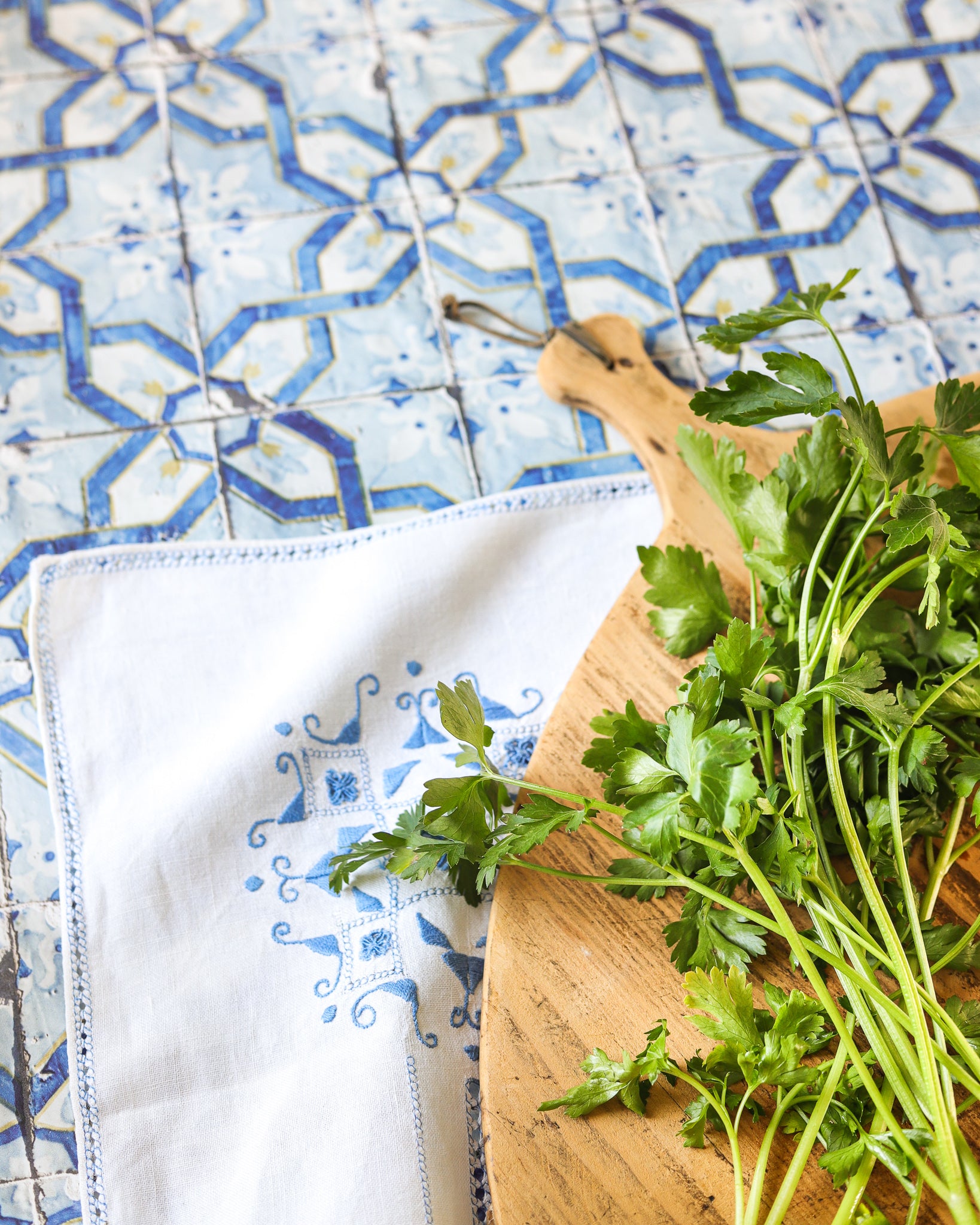 Fresh green herbs on a wooden cutting board against a vinyl photography backdrop featuring a Portuguese azulejo geometric tile pattern in blue, white and yellow.