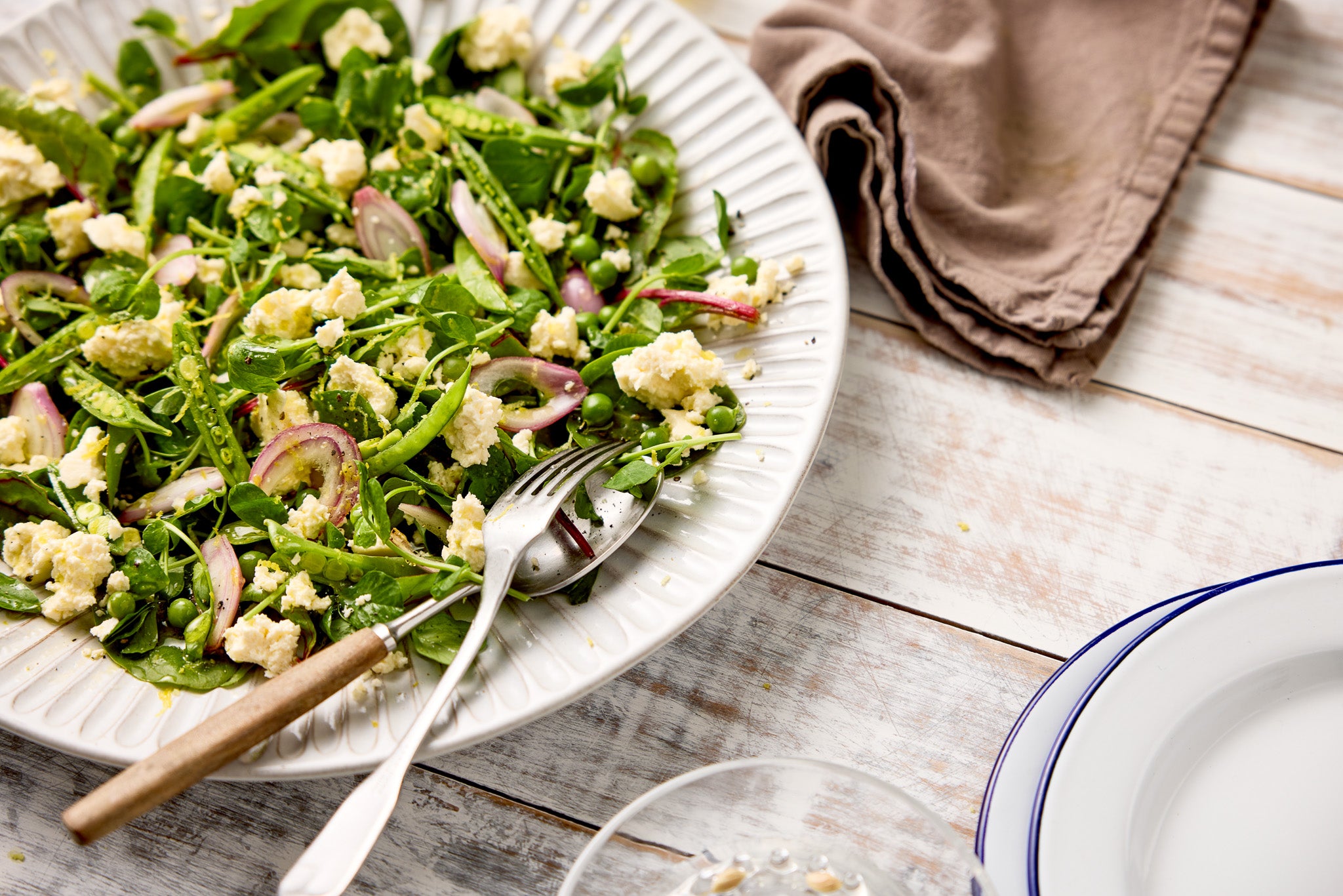 Close-up image of a green salad styled on a white and grey wood plank effect photography backdrop.