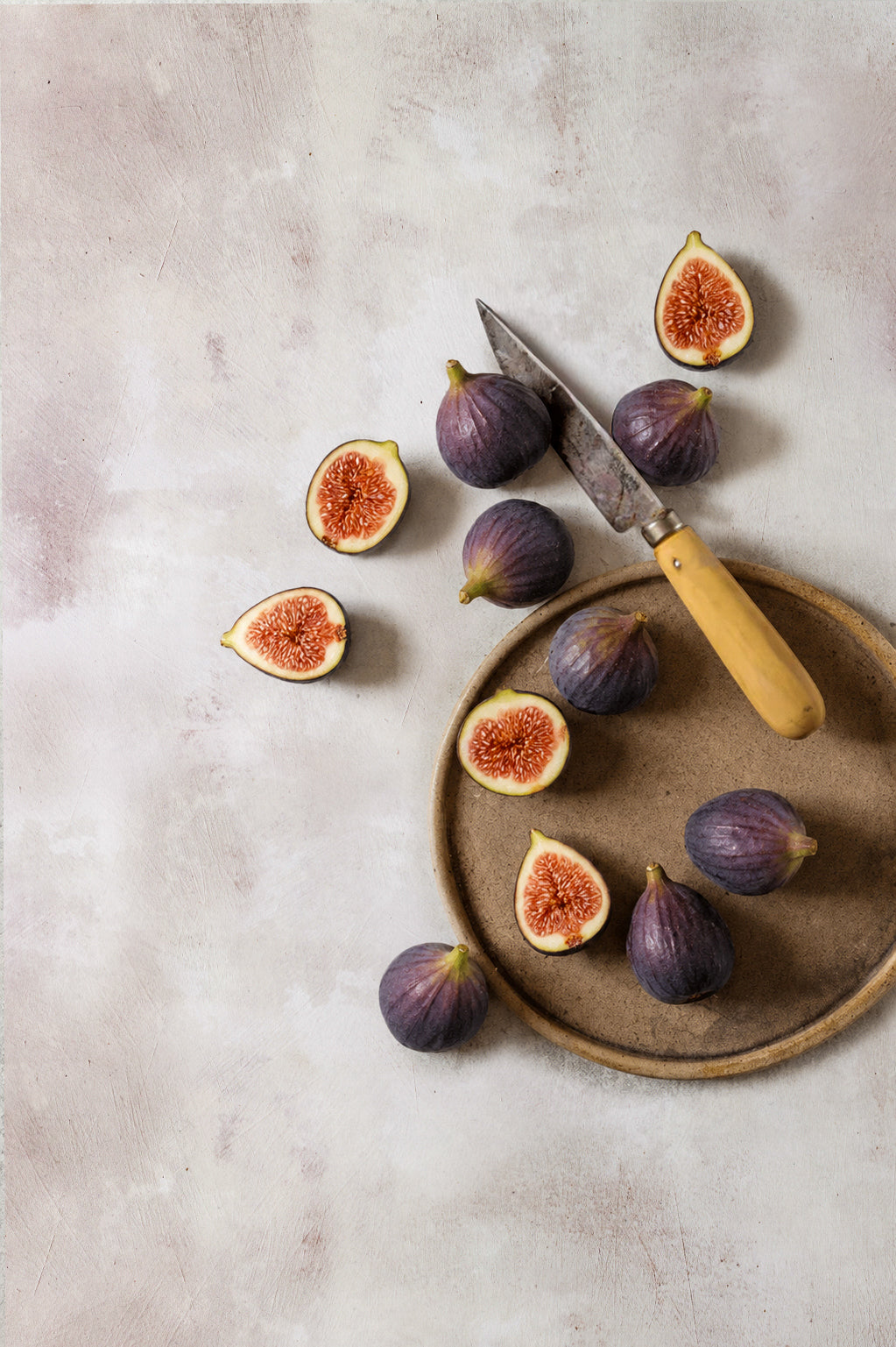 Figs on a plate with a Palleres knife against an off-white plaster effect vinyl photography backdrop.