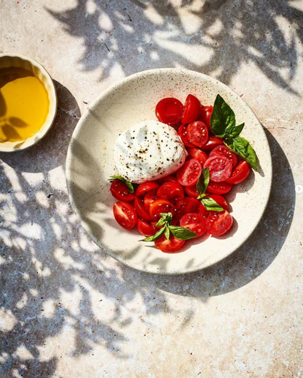 Platter of sliced tomatoes with a ball of mozzarella cheese on a travertine effect vinyl photography backdrop in beige tones.