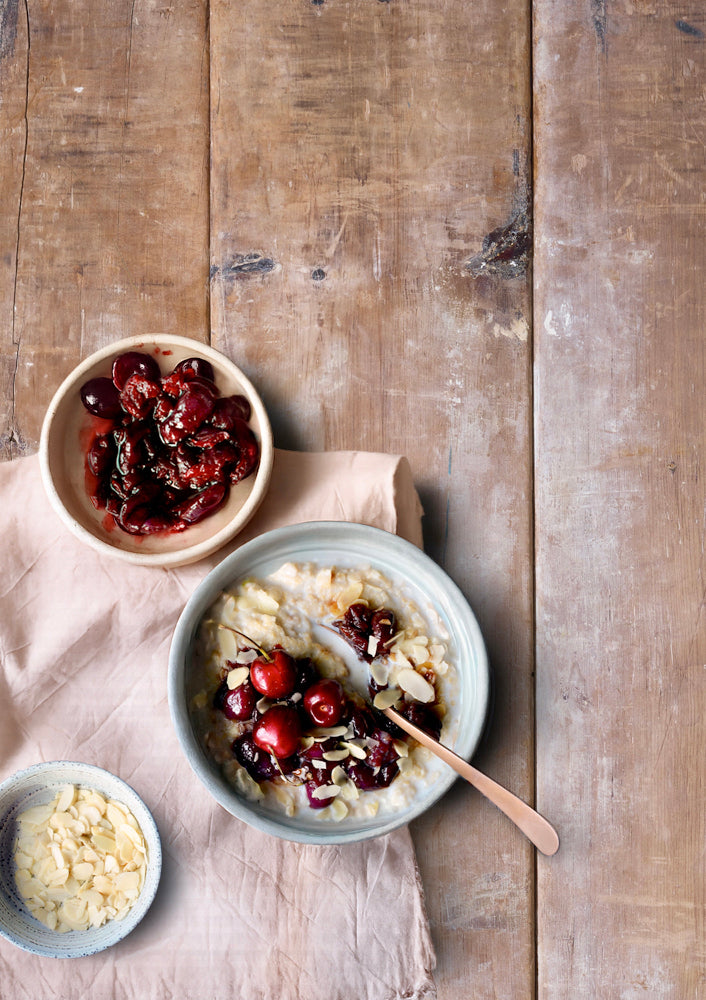 Bowl of porridge with cherries styled on a vinyl photography backdrop captured from an antique wood board with visible wood grain, knots and cracks.