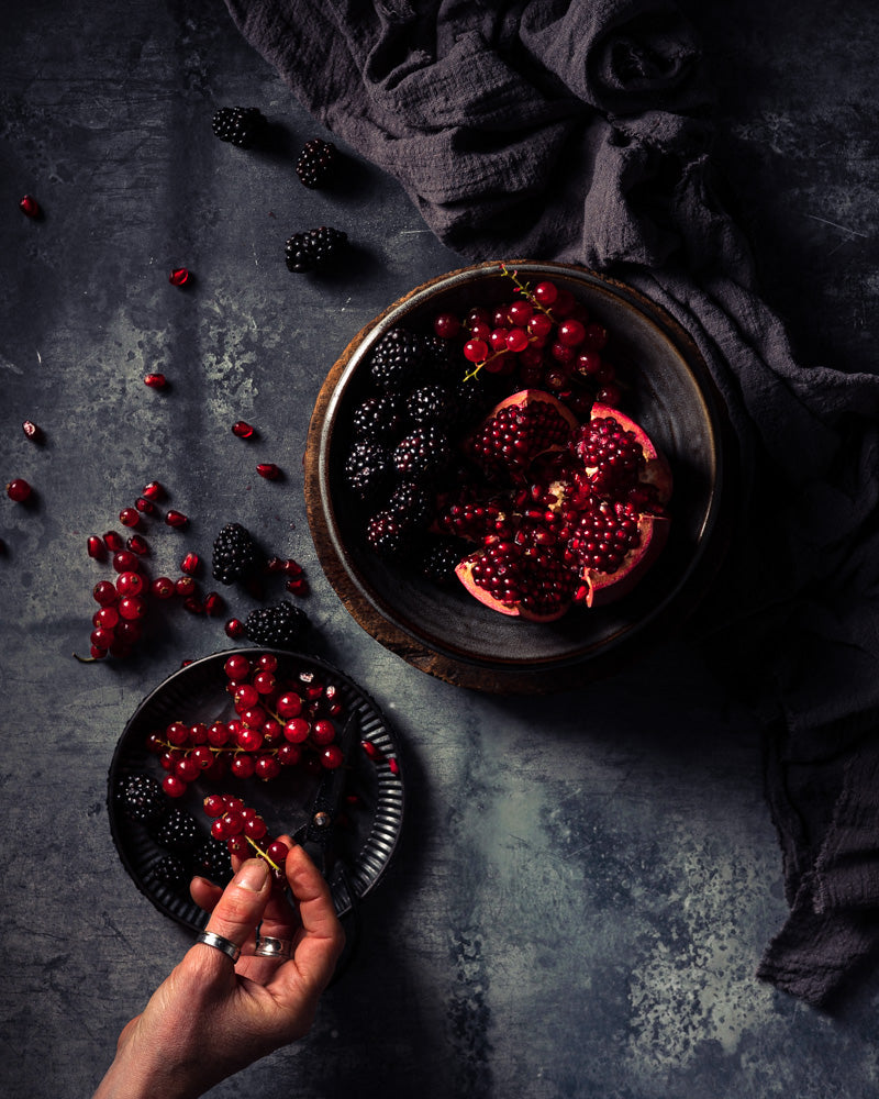 Forest Fruit berries blackberry pomegranate and redcurrants on a flat lay grey blue mottled food photography backdrop.
