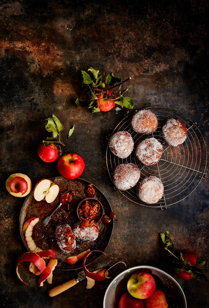A vinyl photography backdrop for food, product and portrait photography in dark and warm brown mottled tones, styled with a rustic flay of apple donuts.