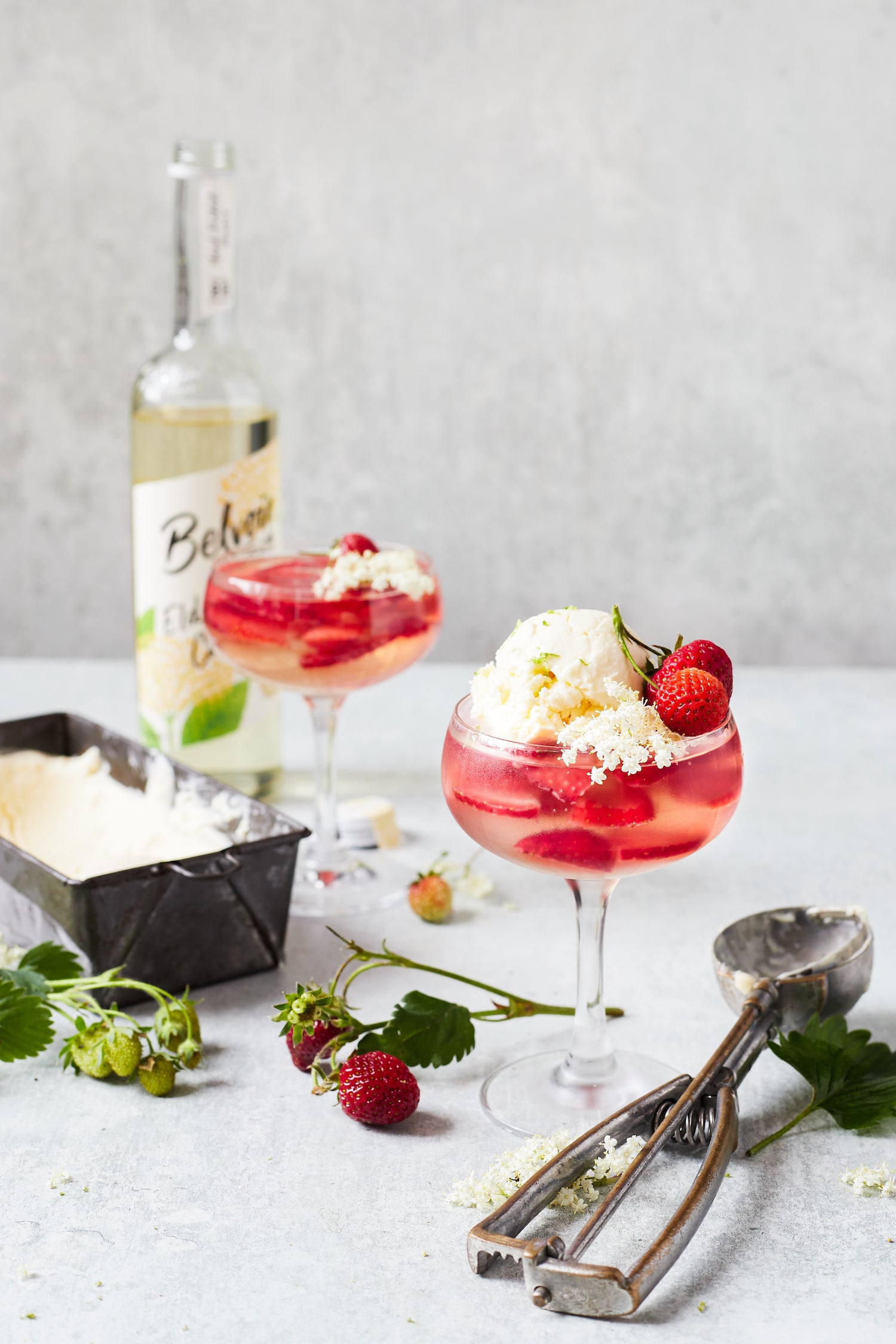 Styled elderflower and strawberry jellies in coupe glasses styled on a textured grey photography backdrop with a concrete effect.