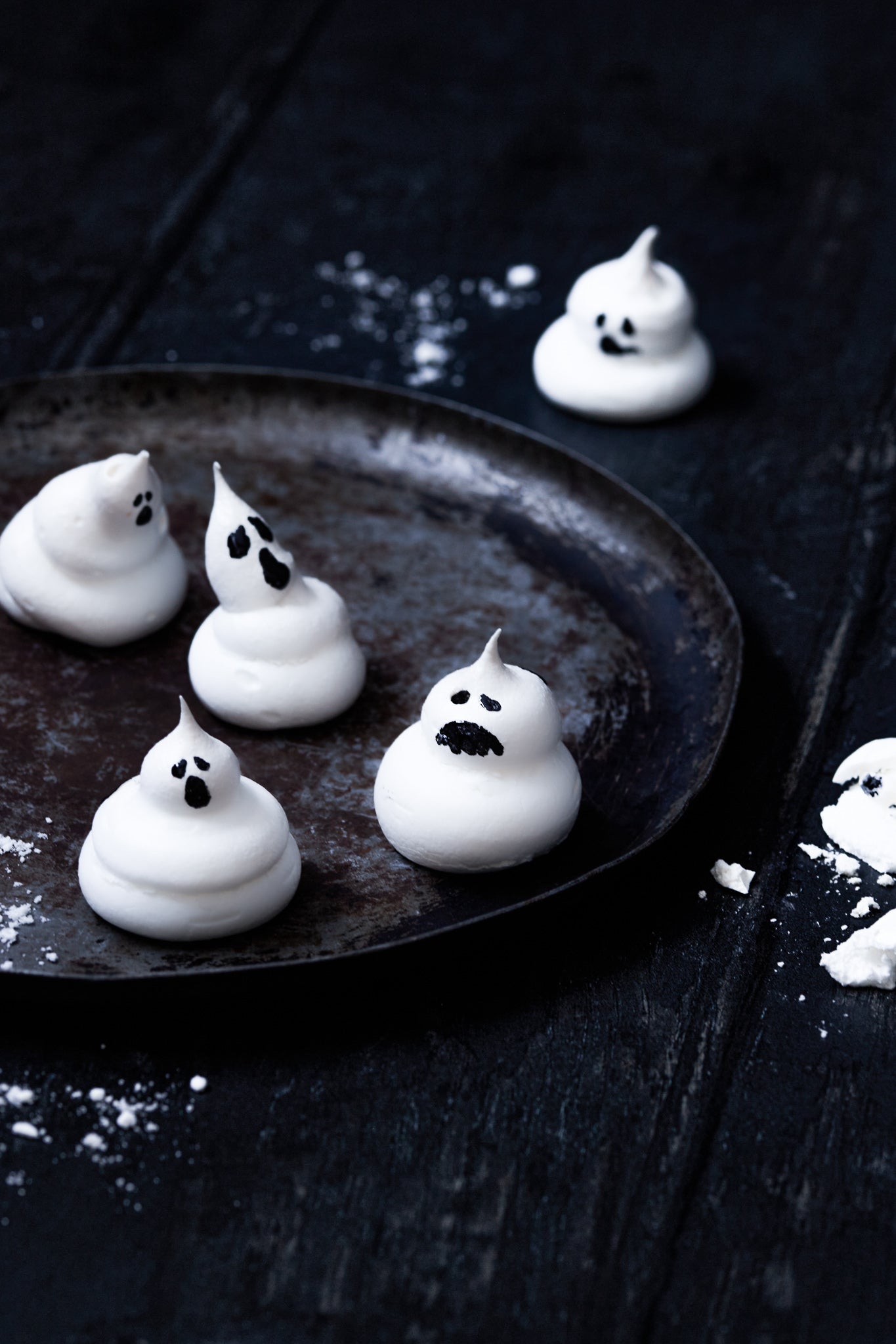 A styled shot of Halloween meringue ghosts on a vinyl food photography backdrop featuring an old dark wood panel effect.
