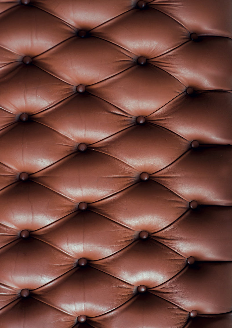 A close-up image of a tan leather effect photography backdrop with button details, resembling a Chesterfield sofa.