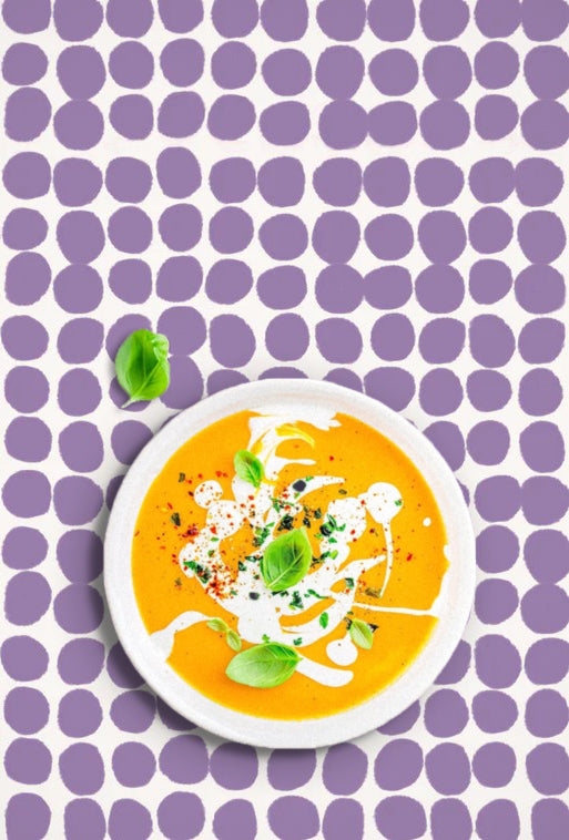 Plate of soup with garnishes on a purple polka dot vinyl photography backdrop with an off-white background.