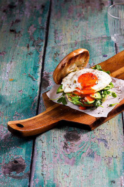 A board with an open egg burger styled on a green flaky wood plank effect vinyl photography backdrop with a textured surface.