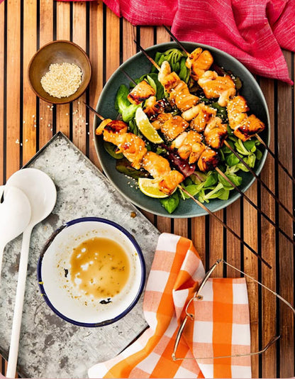 Plated dish of fried chicken skewers with salad on a wooden table effect backdrop
