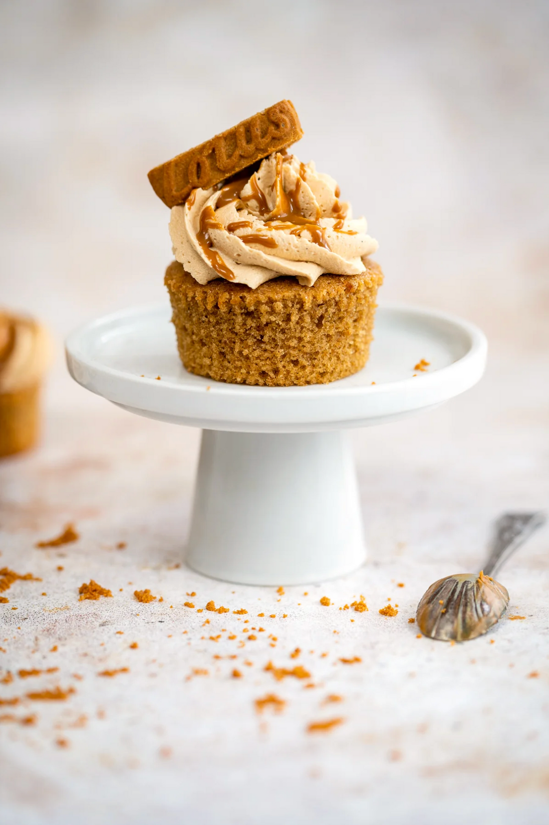 Styled Biscoff cupcake on a white stand against a mottled warm beige vinyl photography backdrop.