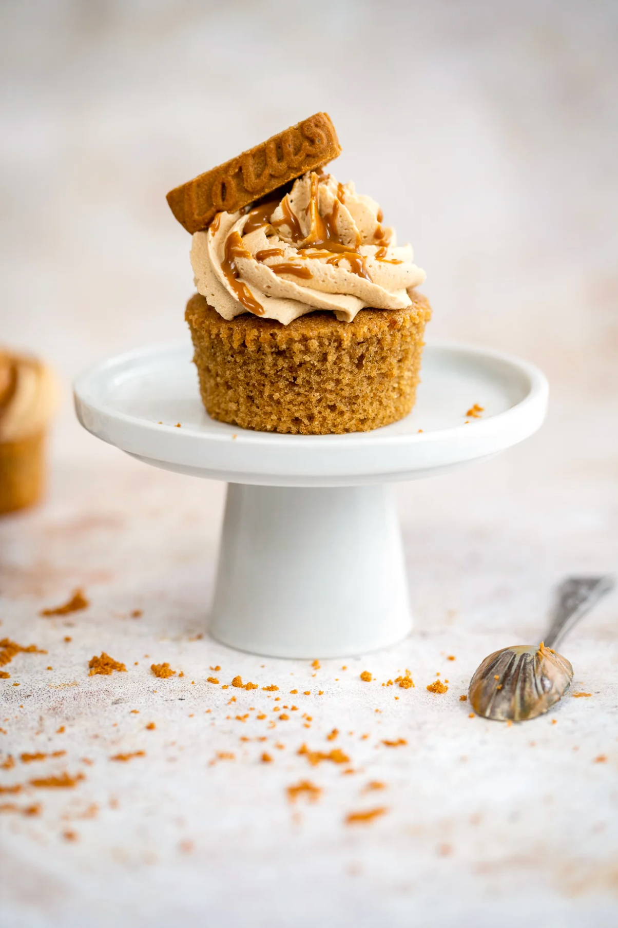 Styled Biscoff cupcake on a white stand against a mottled warm beige vinyl photography backdrop.