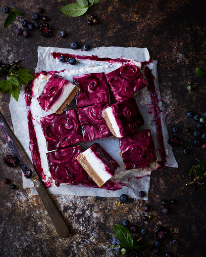 Flat lay of handmade blueberry cheesecake styled on a mottled brown vinyl photography backdrop with dark, umber tones and delicate rusted patches.