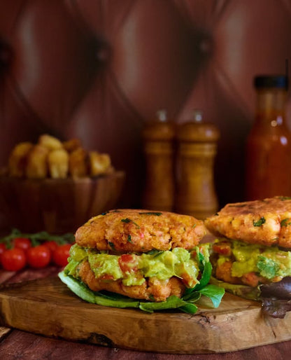 Two salmon burgers with guacamole and lettuce against a tan leather effect photography backdrop with button details, resembling a Chesterfield sofa.