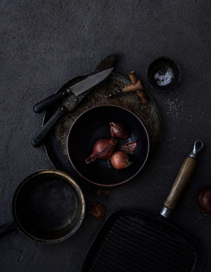 A dark, moody flat-lay of cooking ingredients and utensils on a textured plaster effect dark vinyl photography backdrop for food and product styling.