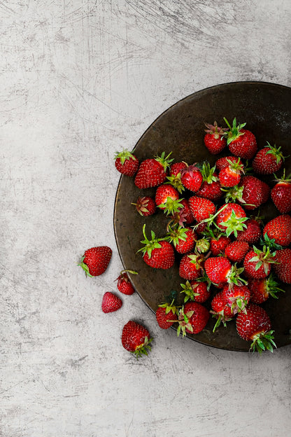 Fresh strawberries on a dark metallic plate shot on an abstract weathered white photography backdrop with grey scratches and a metal patina.