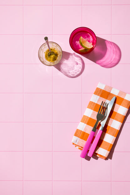 Colourful glassware, checked napkin pink cutlery on a pink tile background