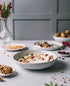 Bowl of yogurt with granola and berries on a table with a gray wall and decorative items in the background.