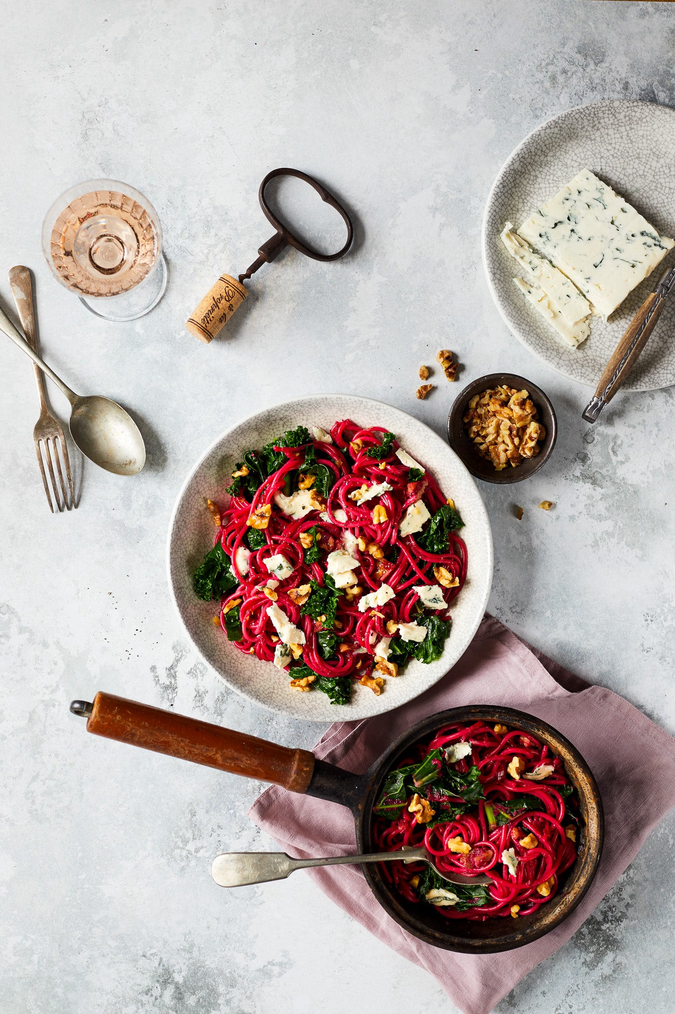 Flat lay  of a bowl of beetroot pasta with food photography props styled on a dappled grey oyster photography backdrop.