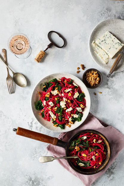 Flat lay  of a bowl of beetroot pasta with food photography props styled on a dappled grey oyster photography backdrop.