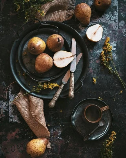 Rustic photography backdrop setting with pears on a dark surface, accompanied by a knife and a cup.