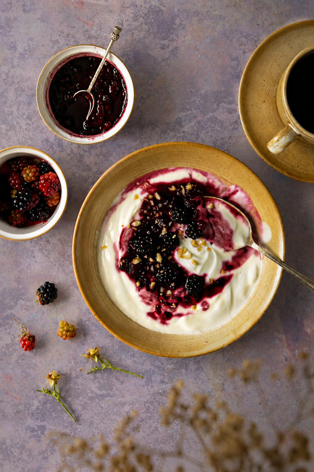 A flat lay of blackberry yoghut and black coffee in French vintage crockery, styled on a light purple and copper effect vinyl photography backdrop.