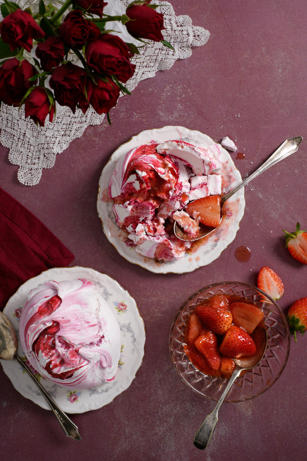 Two vintage side plates with strawberry cloud meringue and a bowl of strawberries styled on a pinkish-red rustic photography backdrop with a real antique plaster-effect.
