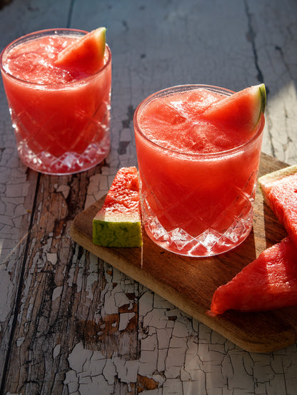 Two glasses of watermelon juice with slices on a white wood rustic photography backdrop.