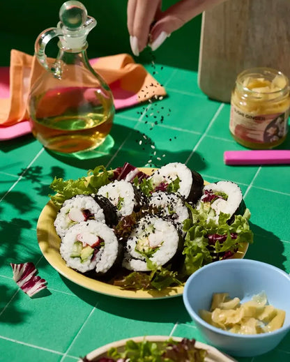 Sushi rolls on a plate with salad and a bottle of oil on a vinyl photography backdrop featuring a graphic tile effect in soft green with white grout lines.