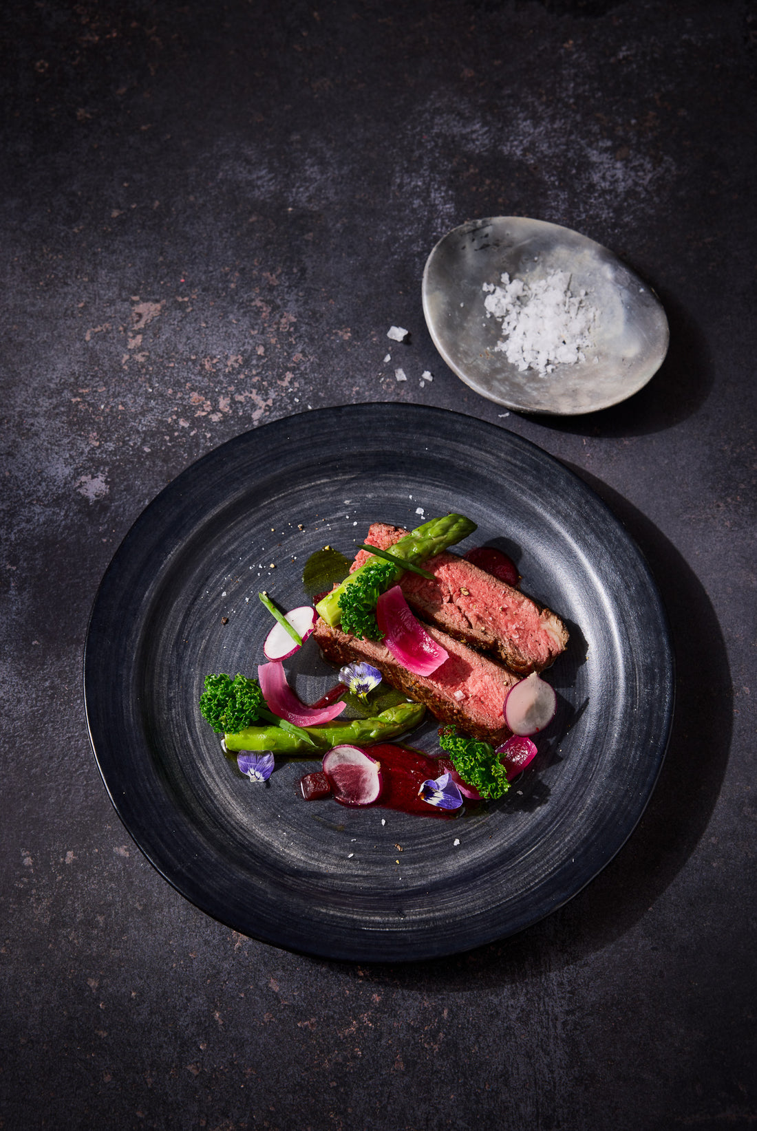 A flat lay of plated meat shot on a vinyl photography backdrop featuring an organic grey stone tile effect.