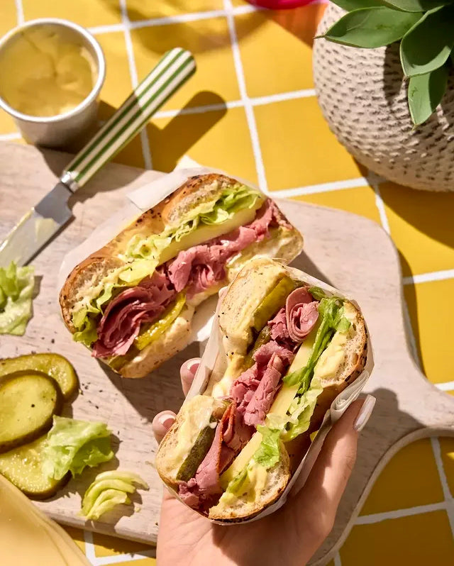 Freshly cut ham and cheese sandwich styled on a yellow tile effect vinyl photography backdrop with white grout lines.