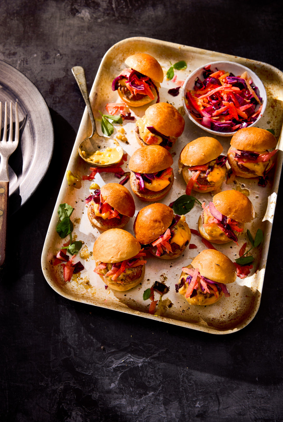 A hand-painted black photography backdrop with a subtle slate-like texture styled with a flat lay of mini burgers in a baking tray