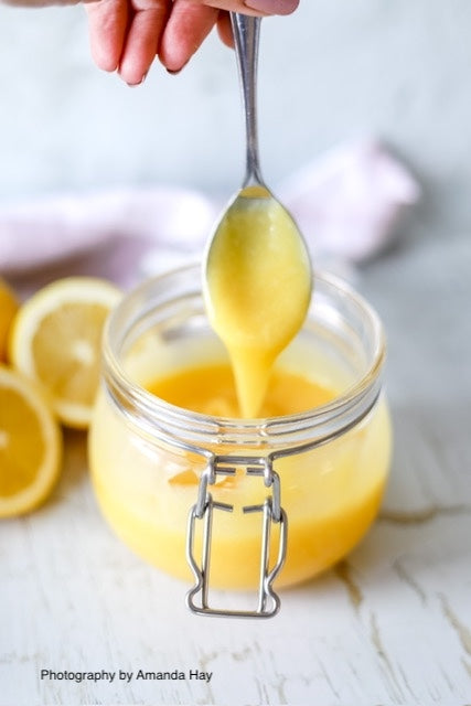 Jar of handmade lemon curd styled on a white wood backdrop