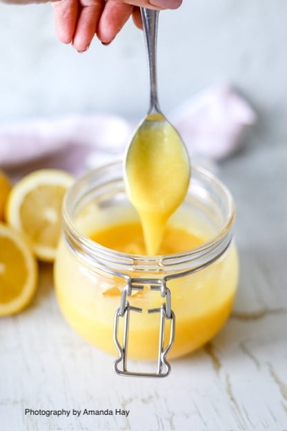 Jar of handmade lemon curd styled on a white wood backdrop