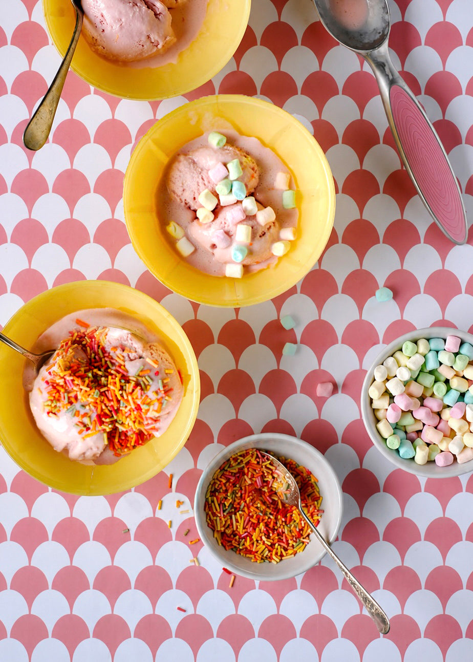 Yellow retro ice cream bowls with colourful toppings on pink and white scalloped pattern vinyl photography backdrop.