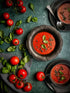 Tomato soup served in a rustic bowl with fresh tomatoes and basil leaves on a green food photography backdrop