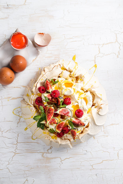 Flat lay of a handmade pavlova styled on a white rustic wood photography backdrop. 