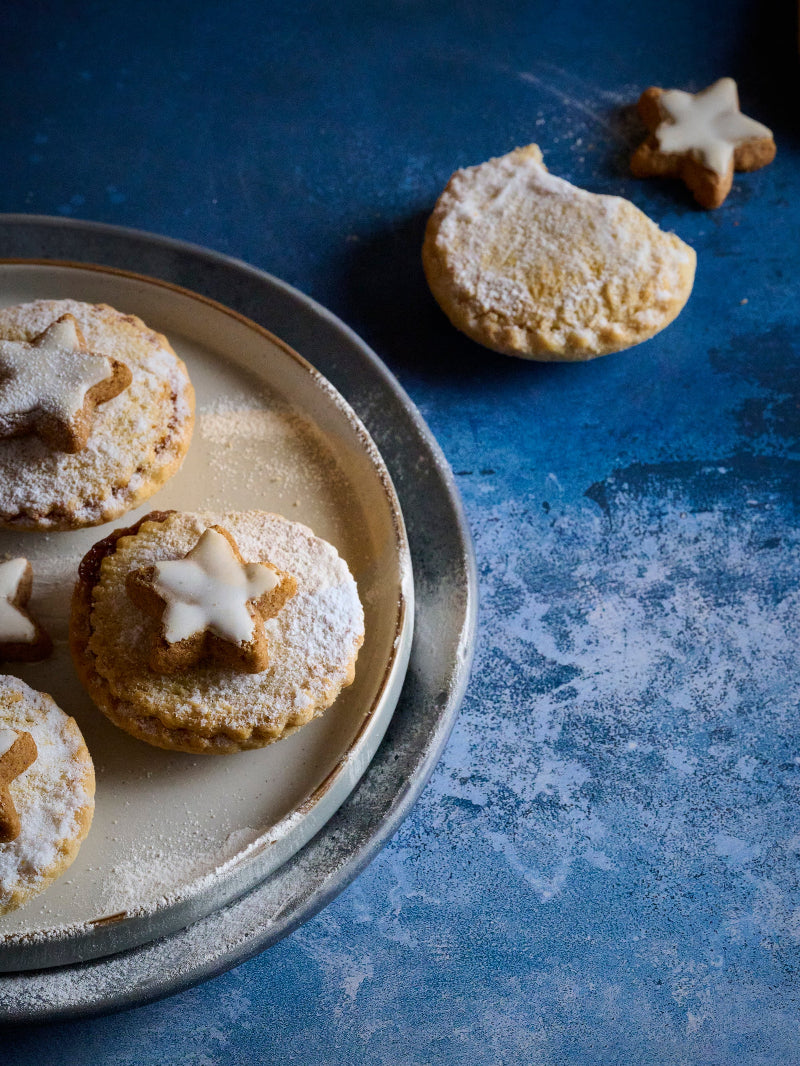 Decorative cookies with star shapes on a plate styled on a vinyl photography backdrop with a gradient of deep blue to frothy white.