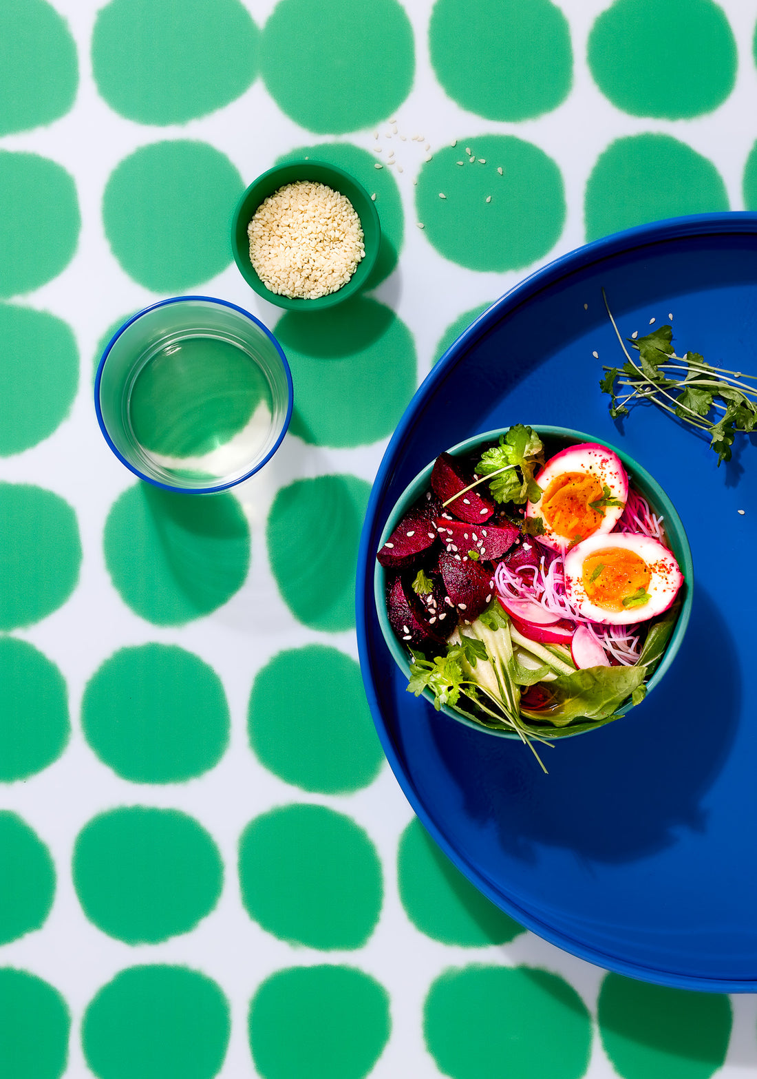 Top down view of a blue tray with a styled egg salad in a green bowl shot on a bright green spotted vinyl photography backdrop.