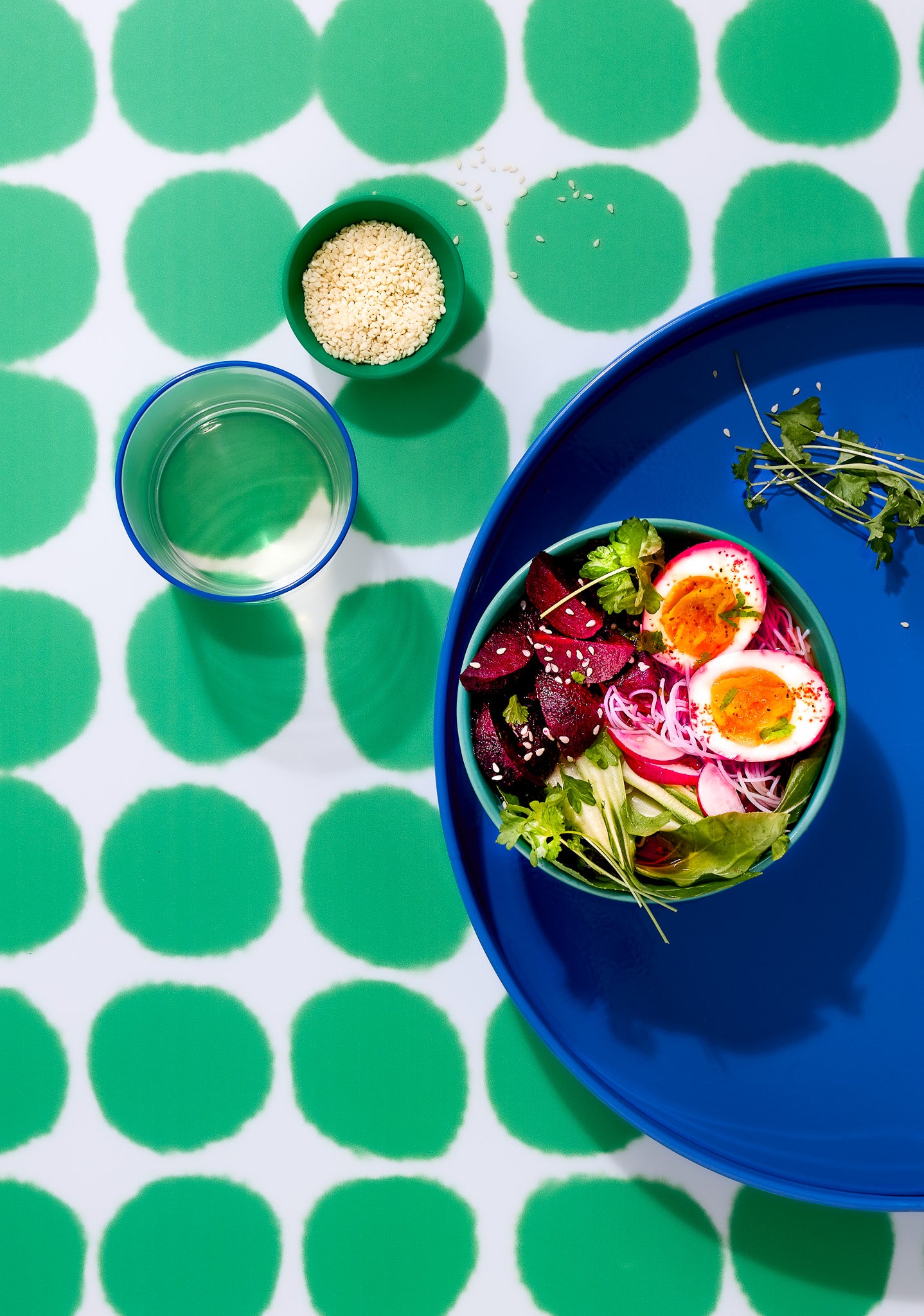 Top down view of a blue tray with a styled egg salad in a green bowl shot on a bright green spotted vinyl photography backdrop.