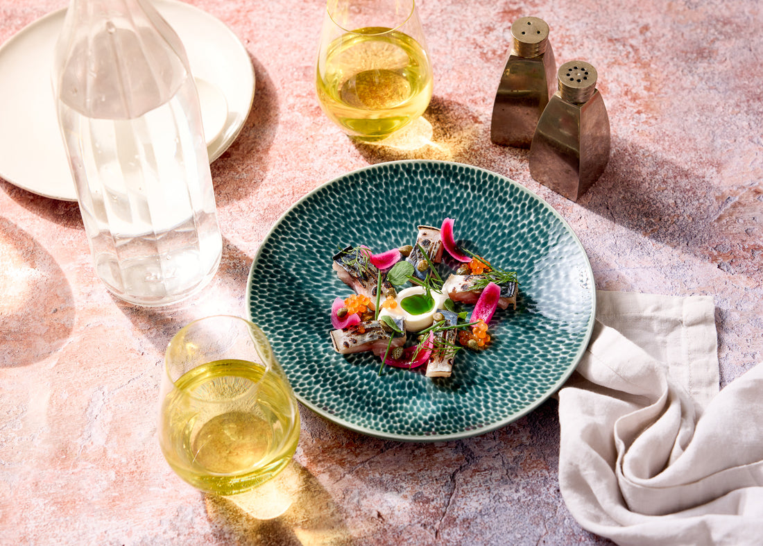 Two glasses of white wine and a colourful plate of food styled on a a natural stone effect warm beige photography backdrop.