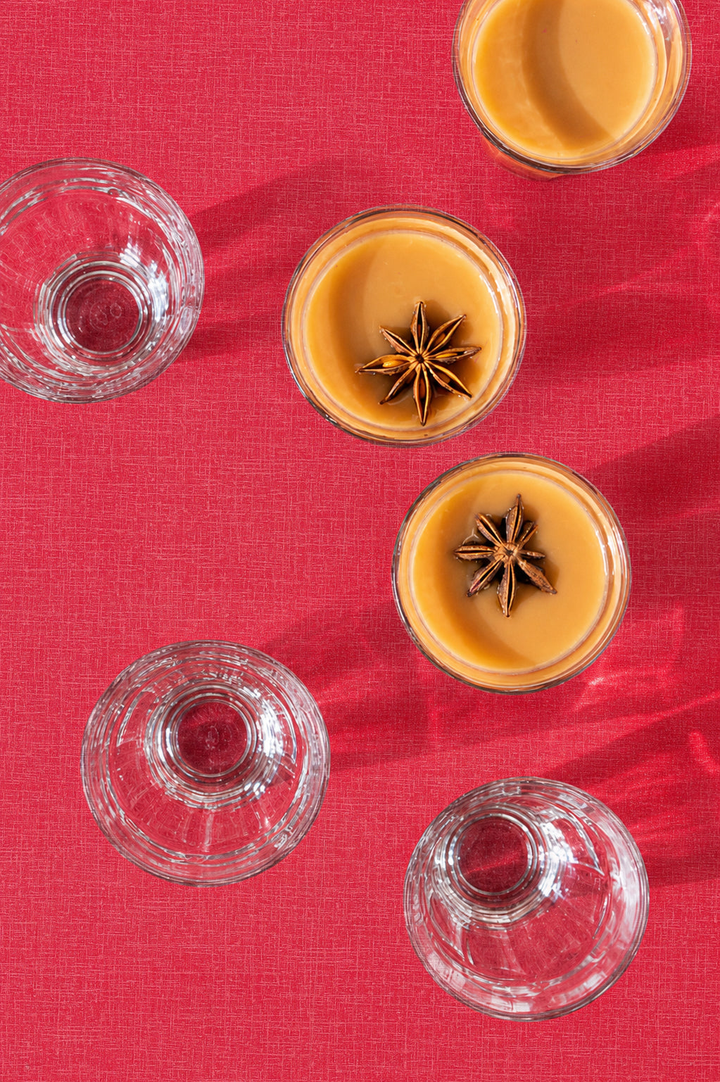 Small glass cups with chai masala and star anise on a red Formica backdrop