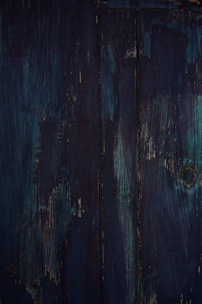 Wood effect vinyl photography backdrop in indigo and near-black tones, with teal tones showing through. Visible brush strokes, scratches and worn patches give it a rustic, painterly and vintage feel. 