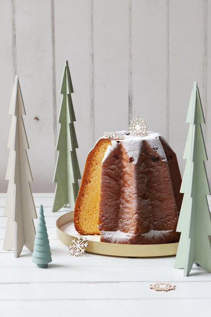 Baked bundt cake with decorative wooden fir trees on a light wood effect vinyl photography backdrop.