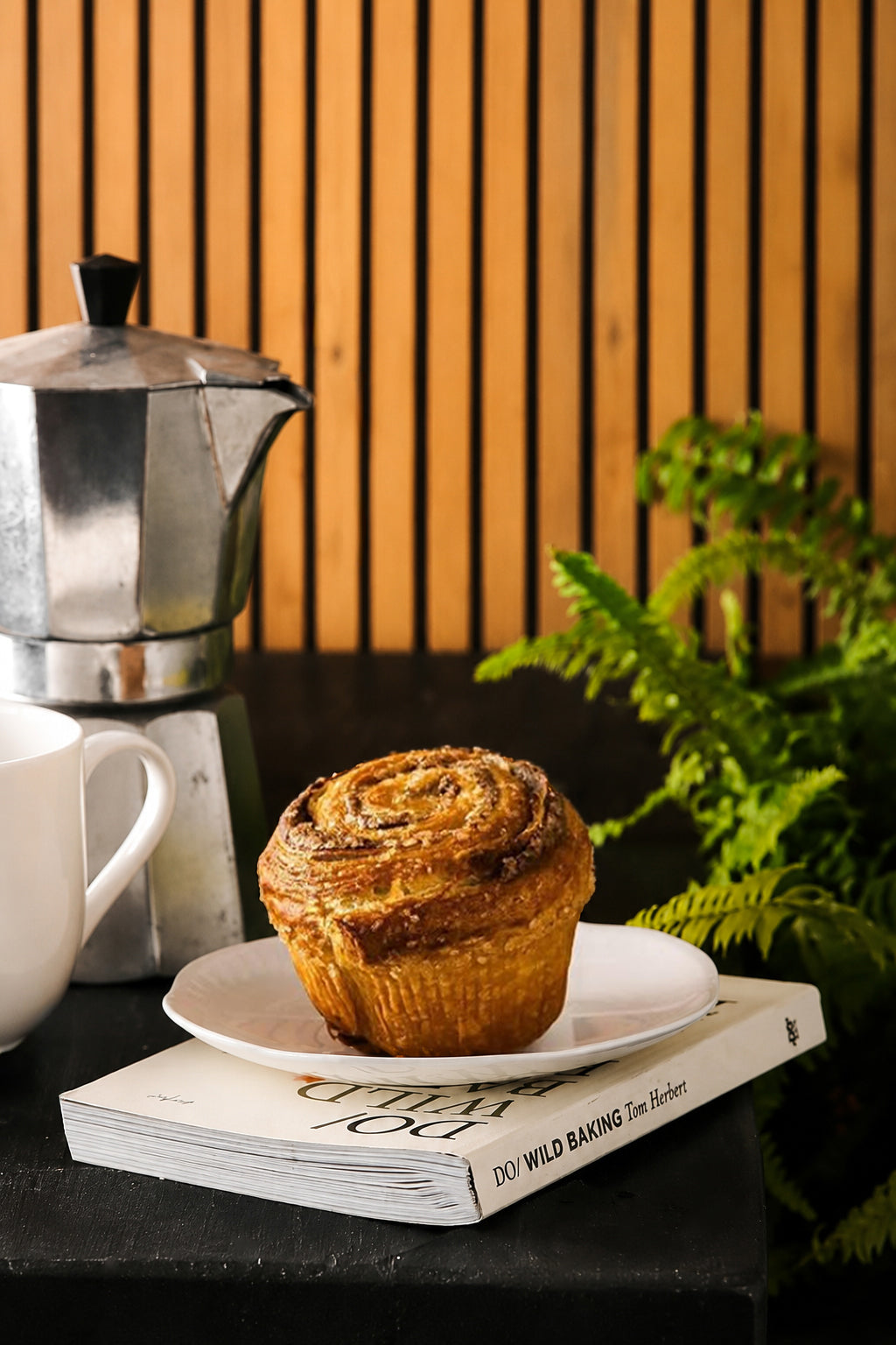 Muffin on a plate with a coffee pot and book against a pine slatted wood panel effect photography backdrop.